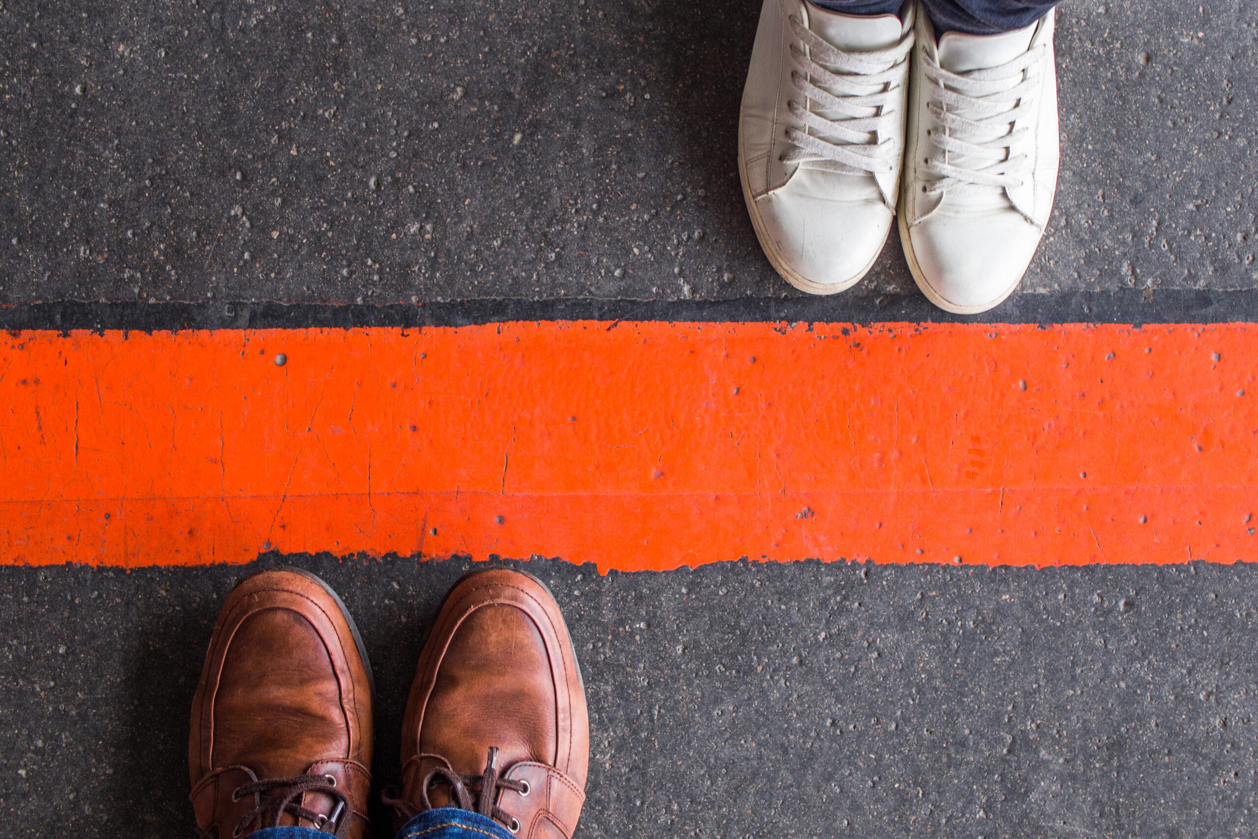 Man and woman standing opposite each other on either side of the road, divided by a red line. Divorce, breakup, borders, barrier and brexit concept.